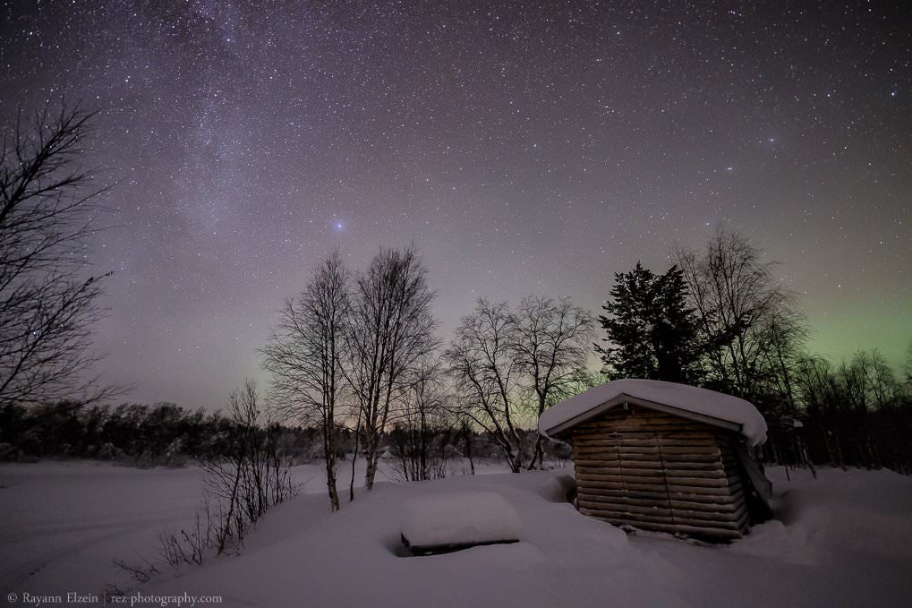 The Milky Way and the Northern Lights above a wood shed