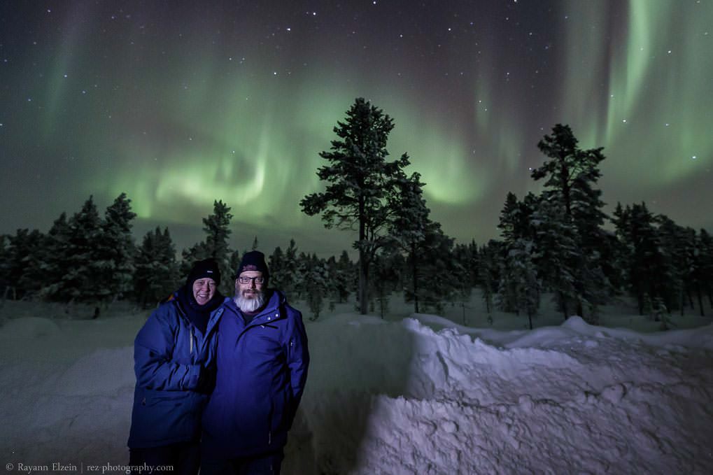 Happy guests during the Aurora excursion around Inari, with strong northern lights dancing in the sky